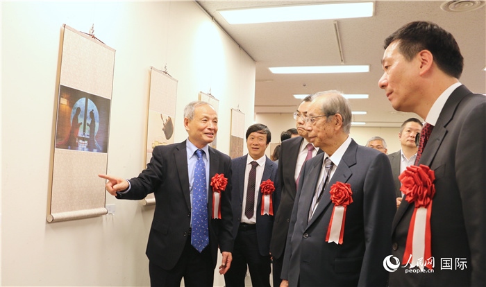 “湖州印象”攝影展主創(chuàng)、世界華人攝影協(xié)會副會長馮學(xué)敏向吳江浩大使、福田康夫前首相等嘉賓介紹展出作品。（人民網(wǎng) 許可攝）