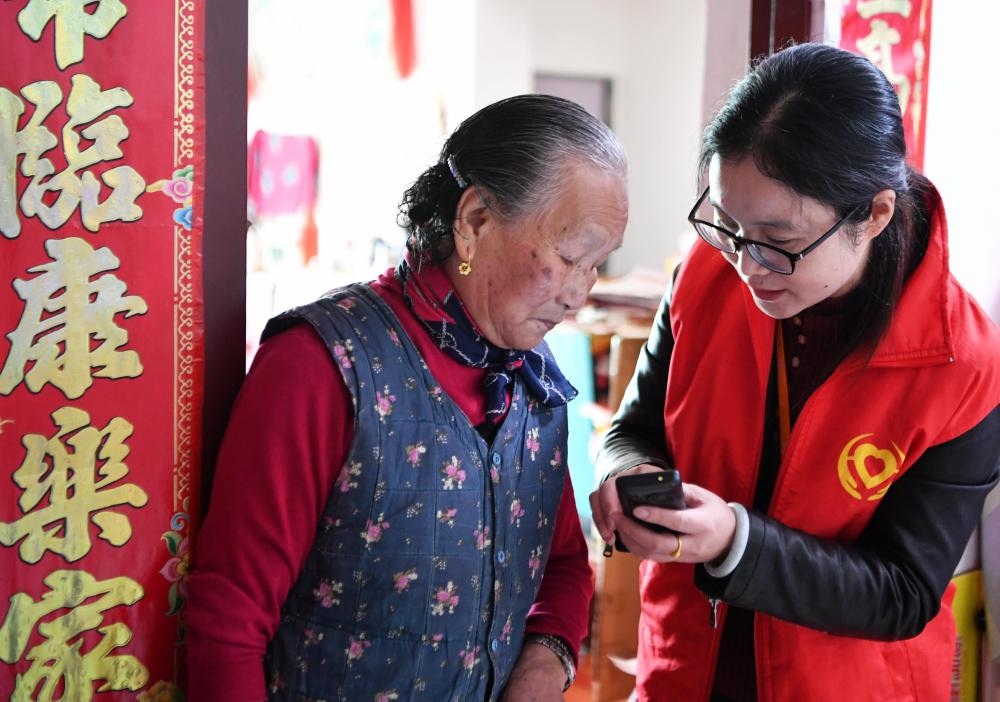 在福州市長樂區(qū)航城街道籌岐村，智慧養(yǎng)老平臺派駐社區(qū)的助老員（右）在為老人陳鳳英（左）講解養(yǎng)老定制手機的用法（2021年11月26日攝）。新華社記者 魏培全 攝