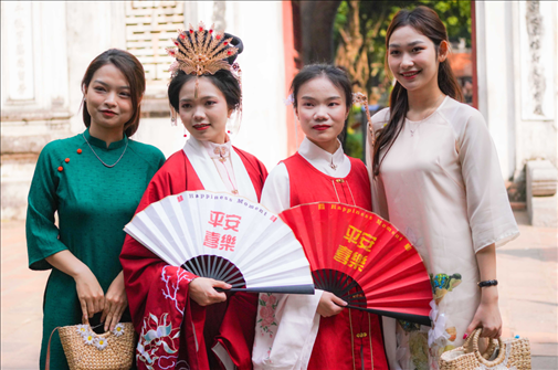 身穿古裝的中國游客和身穿越南傳統(tǒng)服飾奧黛的越南青年在文廟門前合影。