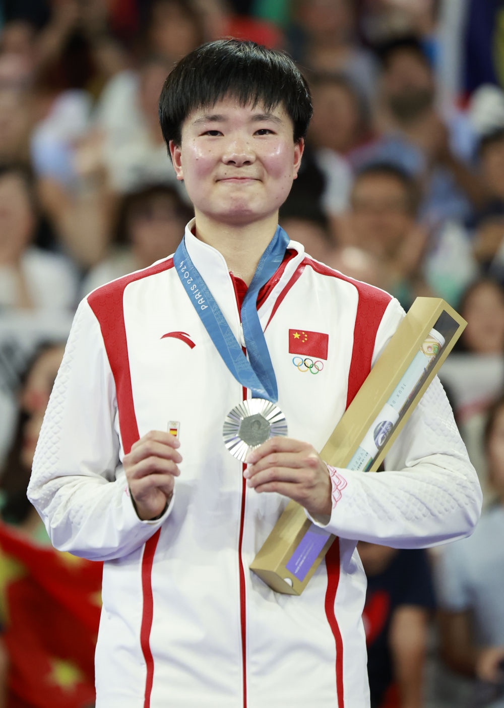 巴黎奧運(yùn)會(huì)羽毛球女子單打亞軍、中國選手何冰嬌在頒獎(jiǎng)儀式上一手握著銀牌，一手握著西班牙奧委會(huì)徽章（2024年8月5日攝）。新華社記者 任正來 攝