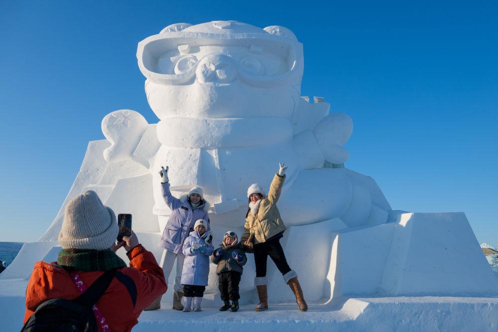2025年1月3日，在黑龍江哈爾濱冰雪大世界園區(qū)，游客與亞冬會吉祥物雪雕“濱濱”合影